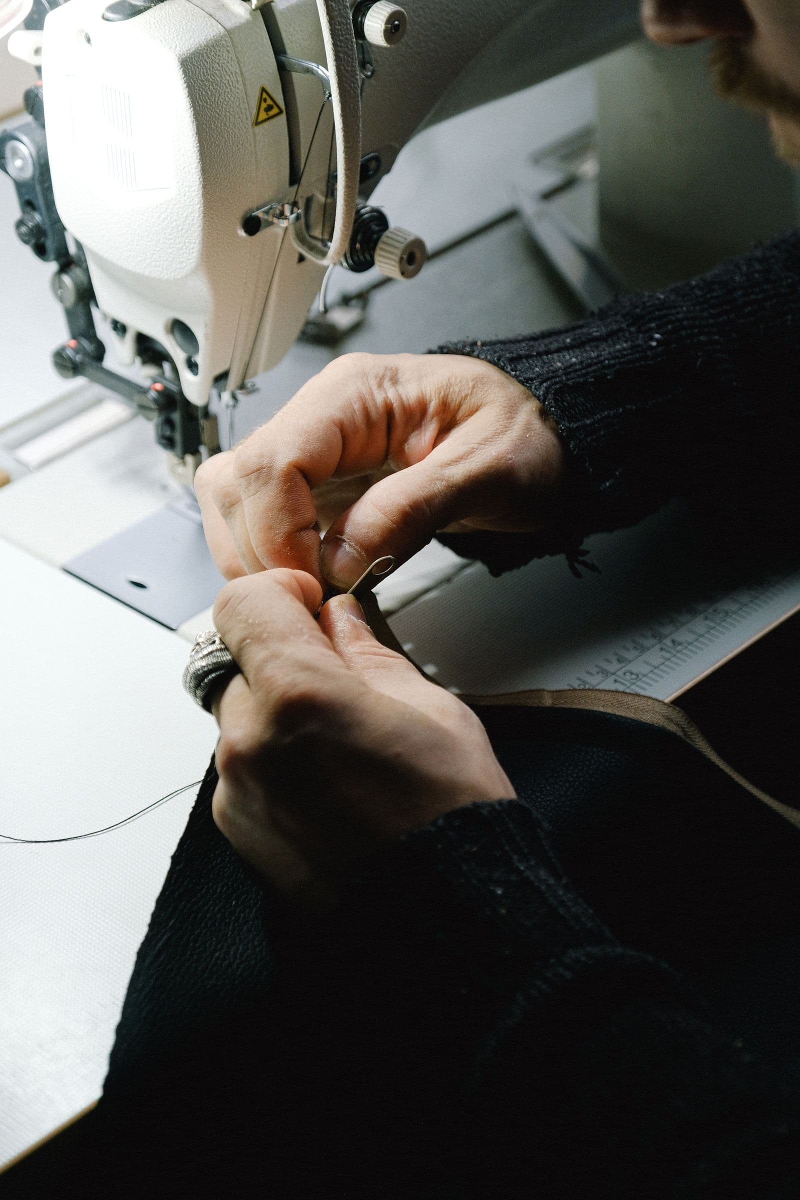 Hands preparing thread beside an industrial sewing machine