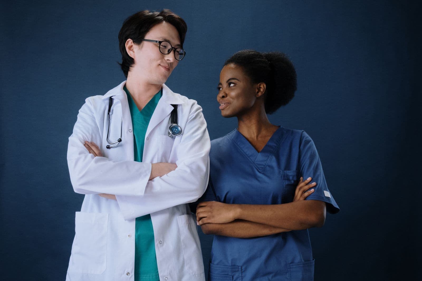 Two healthcare professionals wearing a white coat and blue scrubs against a navy background